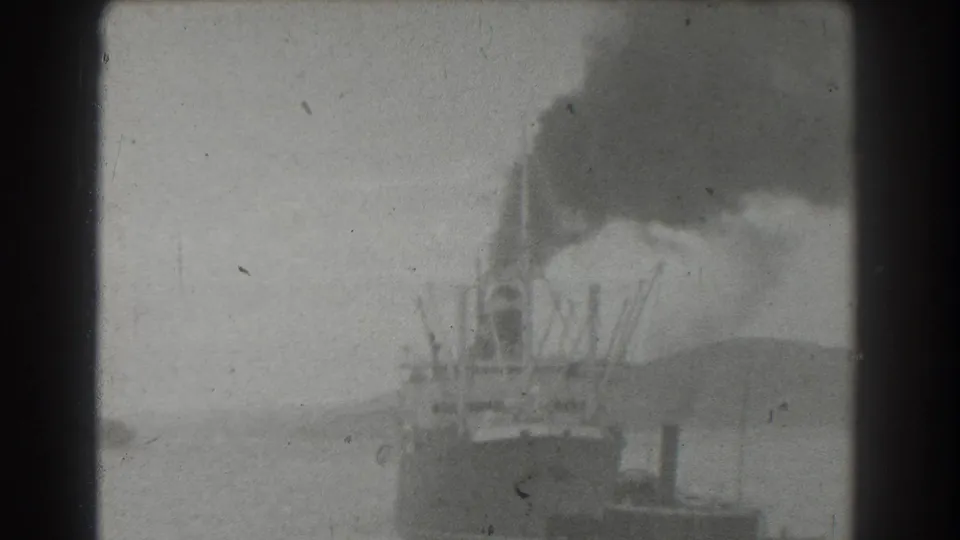 A distant vessel in San Francisco harbor appears beneath a heavy smoke plume, with shoreline shapes faintly visible through aged 8mm film texture.