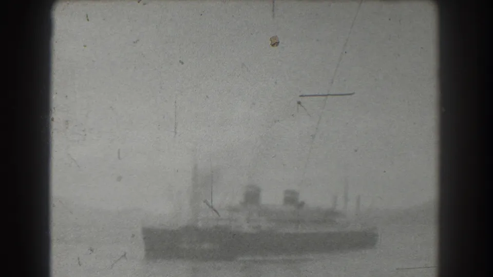 A small tugboat or harbor vessel is seen at a distance on San Francisco harbor water, with smoke haze and aged film marks softening the view.