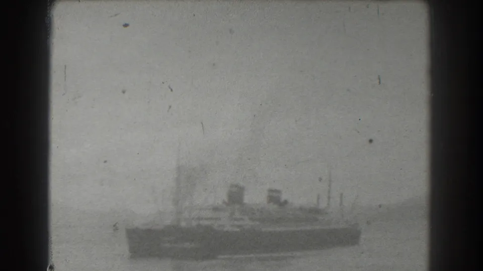 Soft black-and-white 8mm view of a vessel on calm water near San Francisco, with its dark hull, smokestacks, and masts visible against haze.
