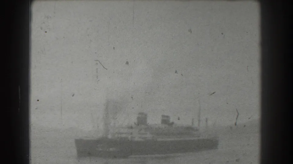 Grainy 1939 home-movie frame showing a distant steamship-like vessel on water, with smokestacks and masts softened by exposure and age.