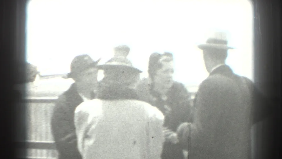 1939 San Francisco home-movie frame showing formally dressed adults gathered near an airfield railing, with bright sky and soft exposure.