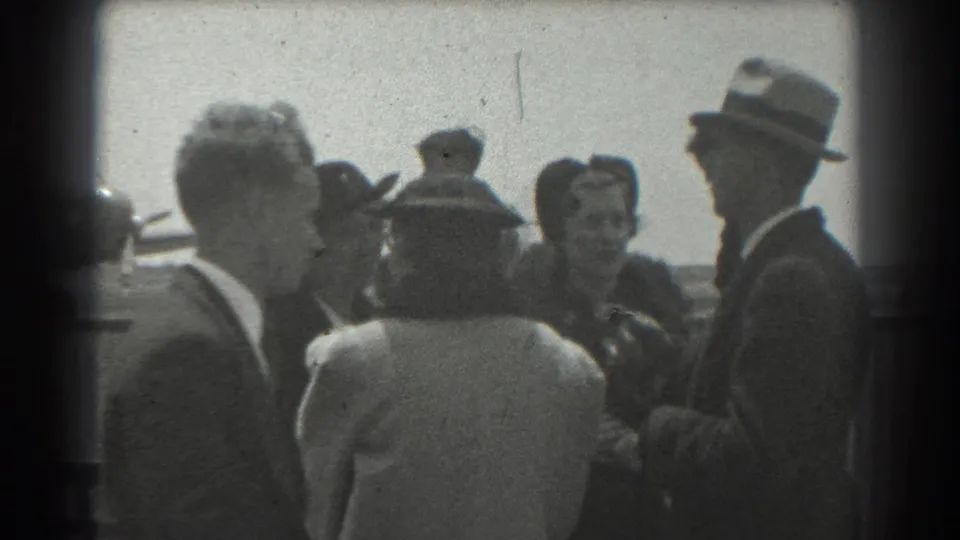 Adults in 1939 San Francisco airfield footage appear to converse, with suits, hats, and a woman smiling in the background.
