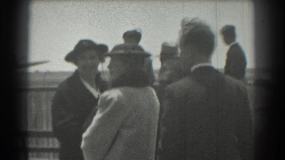 Final 1939 San Francisco airbase frame showing formally dressed adults clustered near the runway area, with soft focus and visible film wear.