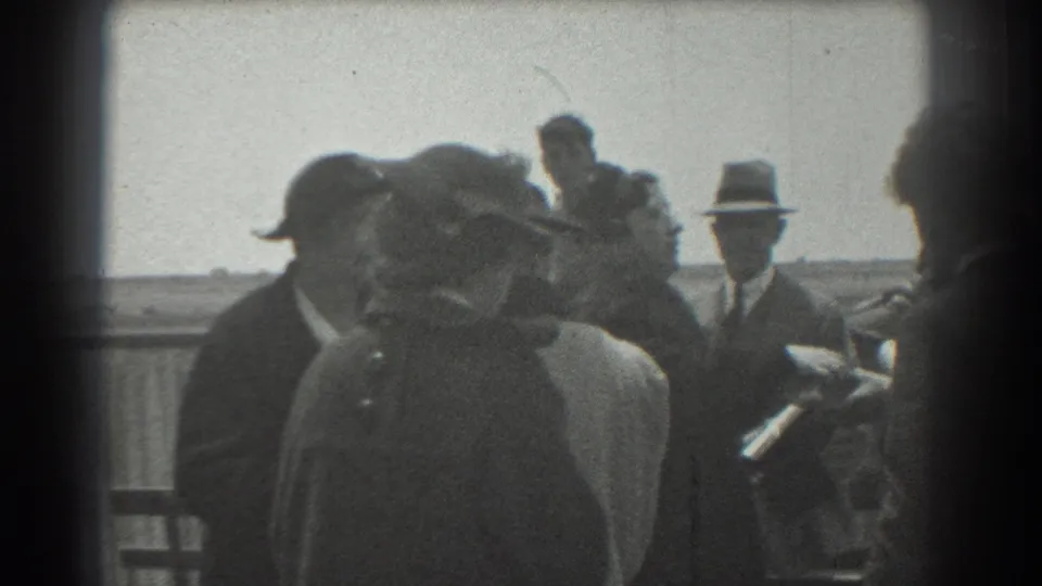 1939 San Francisco 8mm frame showing adults in period hats and coats gathered on an outdoor platform near a railing.