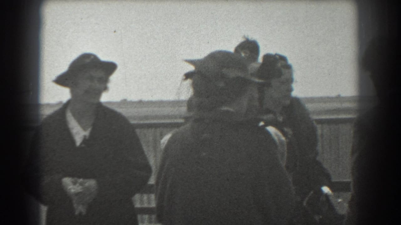 A woman in a dark coat and hat stands beside other adults on the platform.