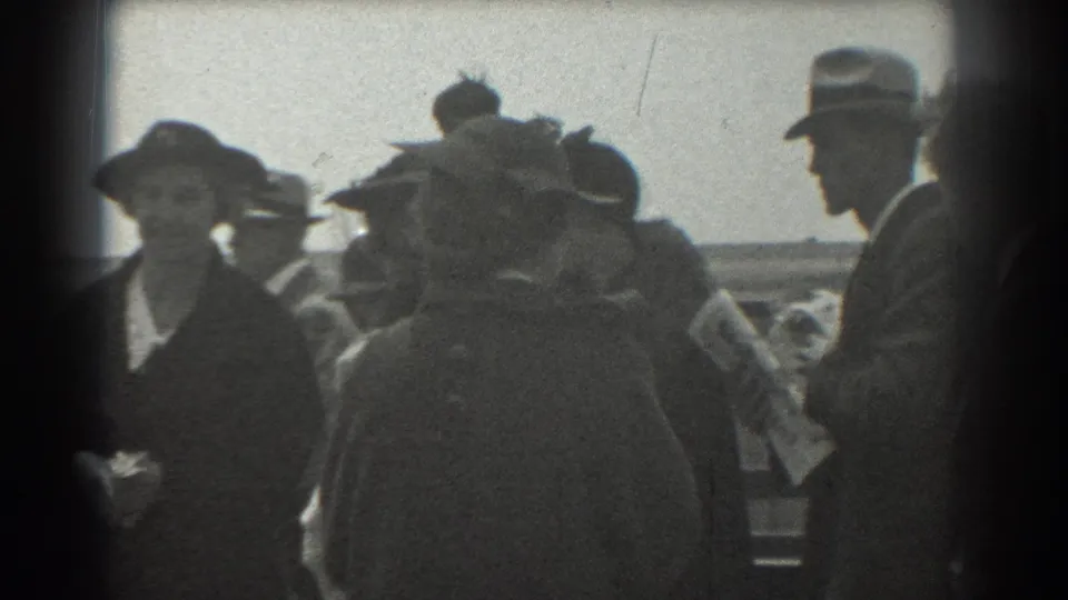 1939 San Francisco 8mm frame with a suited man in a fedora standing near women in hats on a public platform.
