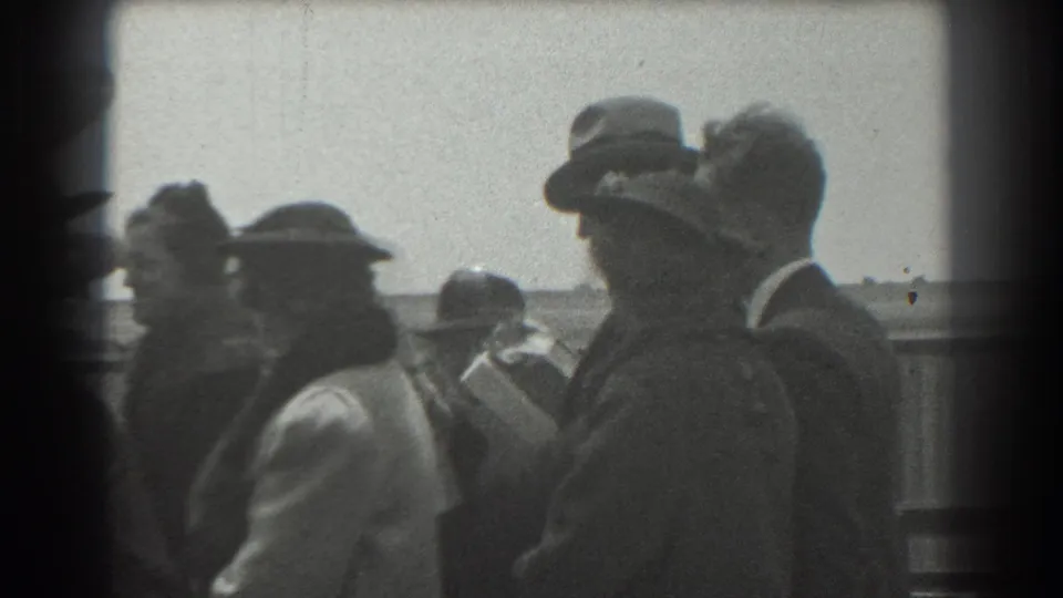 Adults in 1930s attire appear in profile at an outdoor San Francisco gathering, with a fence and open background behind them.