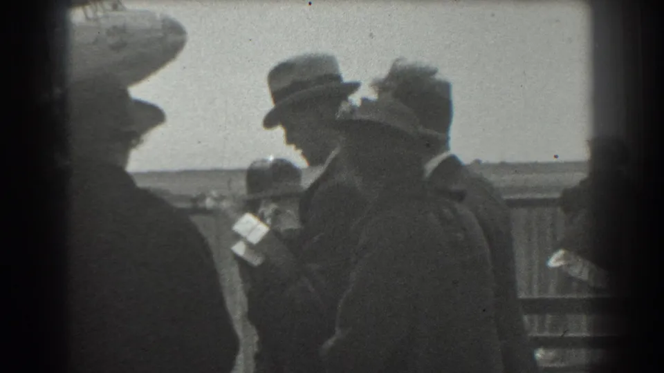 Candid 1939 San Francisco frame showing adults in period hats and coats gathered outdoors beside a fence in soft 8mm focus.