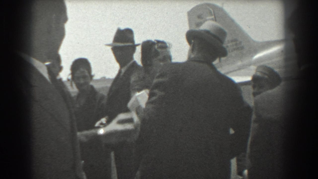Crowd of formally dressed adults standing near an aircraft tail at an airport.