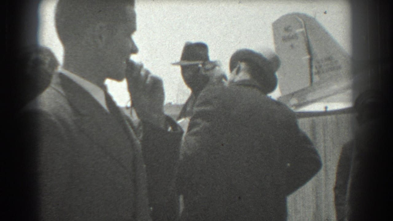 Man in profile smoking while other adults stand near an aircraft tail.