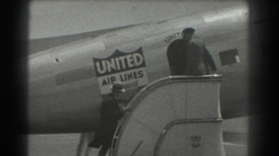 In 1939 San Francisco airport footage, a United Air Lines aircraft fuselage appears beside boarding stairs with people standing on or near the steps.