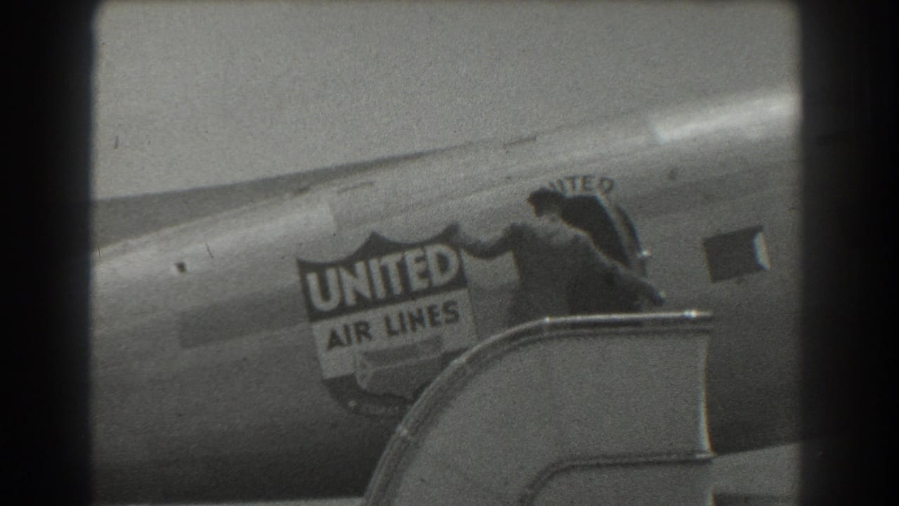 Man in a suit and hat steps from a United Air Lines aircraft near passenger stairs.