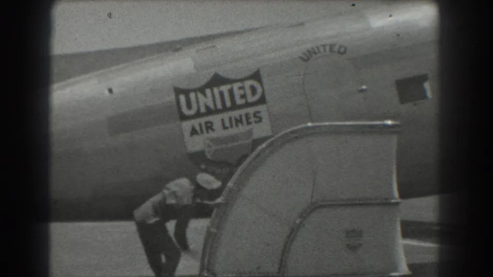 A suited man in a hat is visible low in frame near the passenger stairs, beneath the United Air Lines logo on the aircraft.