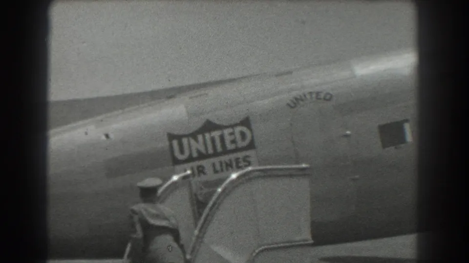 1939 San Francisco home-movie frame showing a United Air Lines fuselage with logo and passenger stairs in soft black-and-white focus.