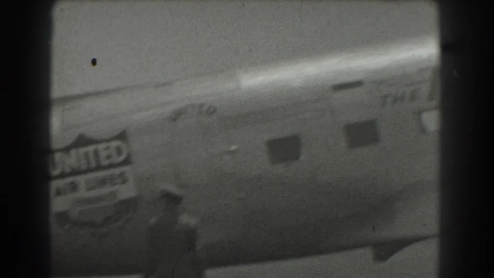 Black-and-white 8mm frame of the United Air Lines fuselage and logo, with a blurred person moving in the foreground.