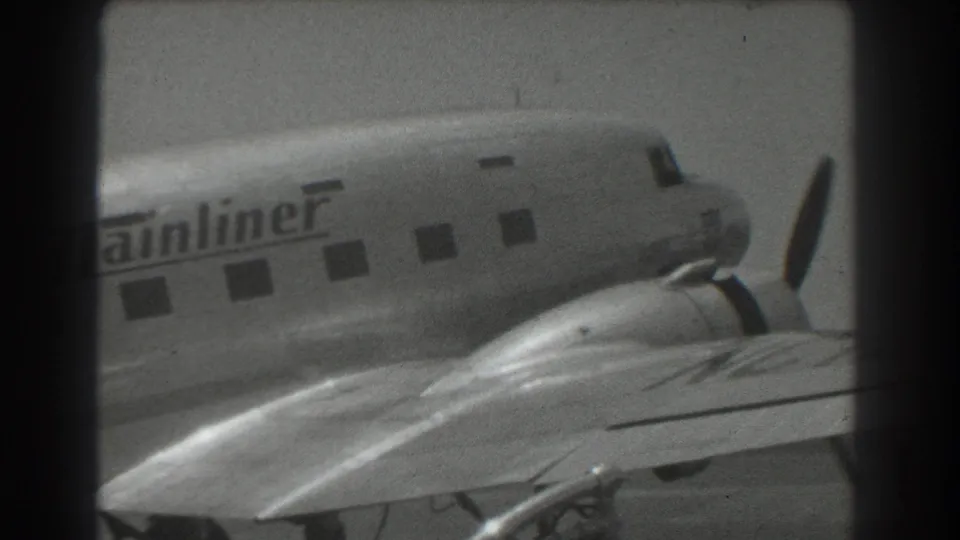 1939 San Francisco home-movie frame showing a propeller airliner's nose area, wing, windows, and partial The Mainliner fuselage lettering.