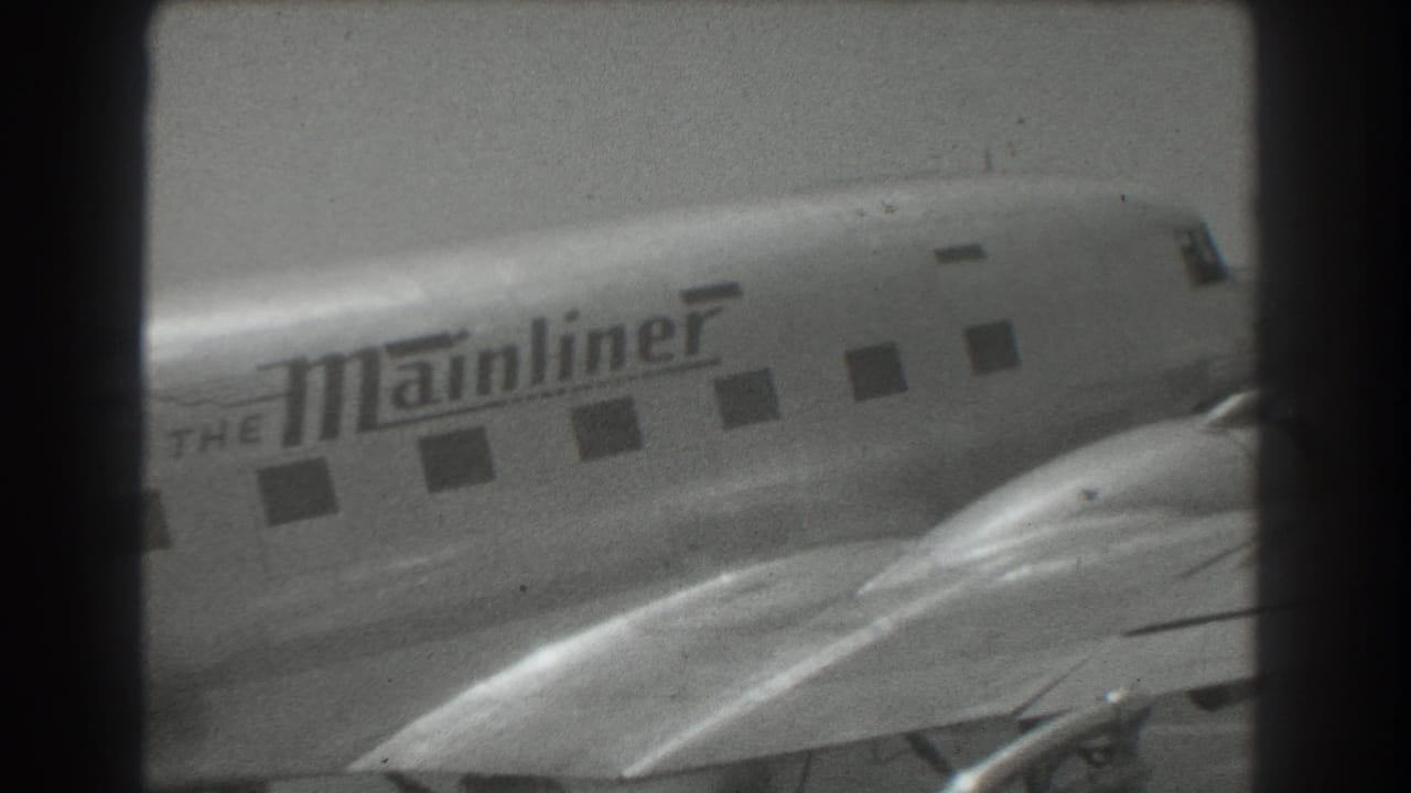 Close view of a propeller airliner fuselage with 'The Mainliner' lettering and passenger windows.