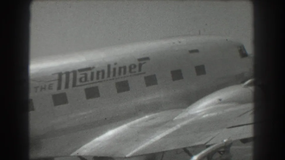 1939 San Francisco home-movie frame showing a close, grainy view of a branded Mainliner propeller airliner on the tarmac.