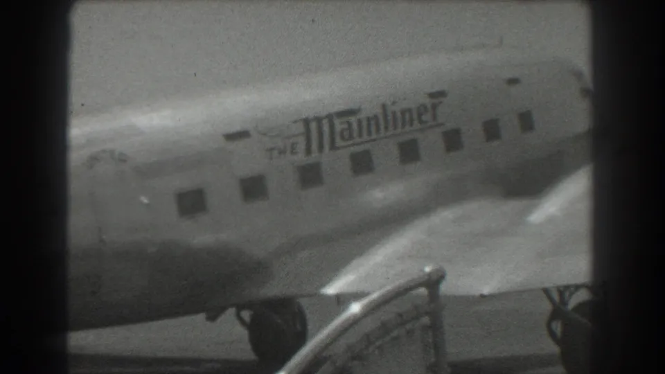 A soft 1939 home-movie frame shows the Mainliner name, aircraft windows, wing area, and tarmac equipment in front.