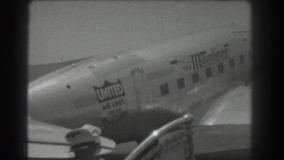 Black-and-white 8mm view of a United Air Lines DC-3 Mainliner at a San Francisco airport, with railing and wing edge visible.