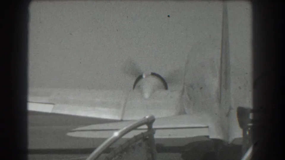 Black-and-white 8mm frame from 1939 San Francisco showing a propeller aircraft tail, wing, and rotating propeller blur.