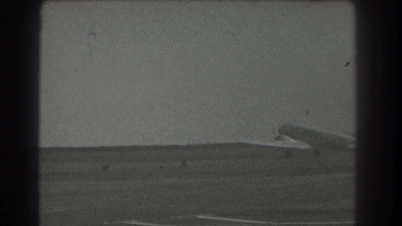 Small aircraft near the runway horizon, framed by dark 8mm film borders.