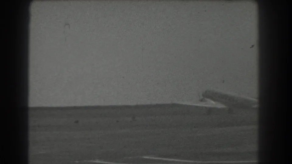 A distant propeller aircraft appears near the horizon at a San Francisco-area airfield in this 1939 black-and-white 8mm frame.