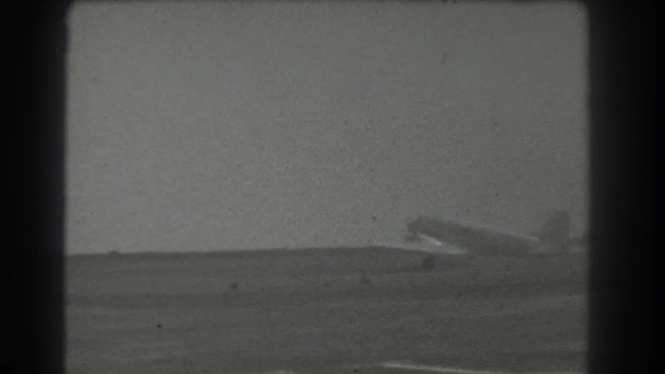 1939 San Francisco-area 8mm frame showing a light-colored propeller airplane positioned on a runway in the distance.