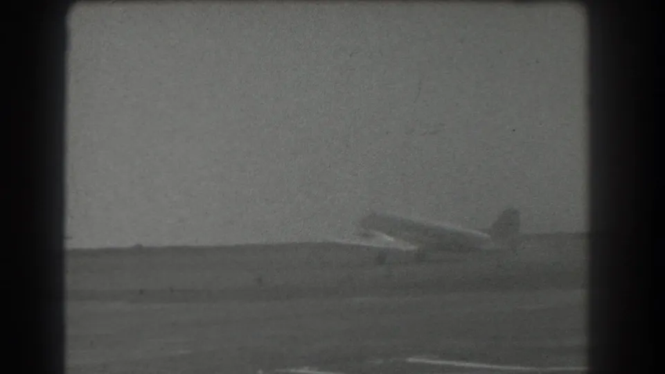 Distant 8mm frame of a light propeller aircraft on a San Francisco-area runway, with soft grain and dark frame edges.