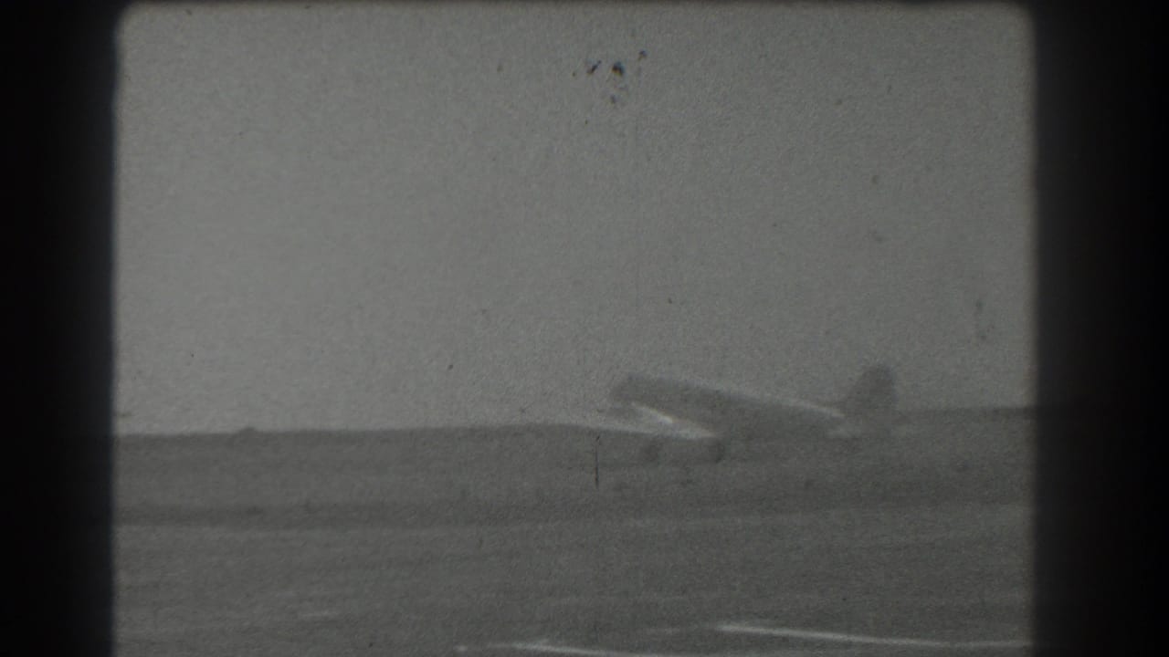 Distant airplane on an open airfield under a cloudy sky.