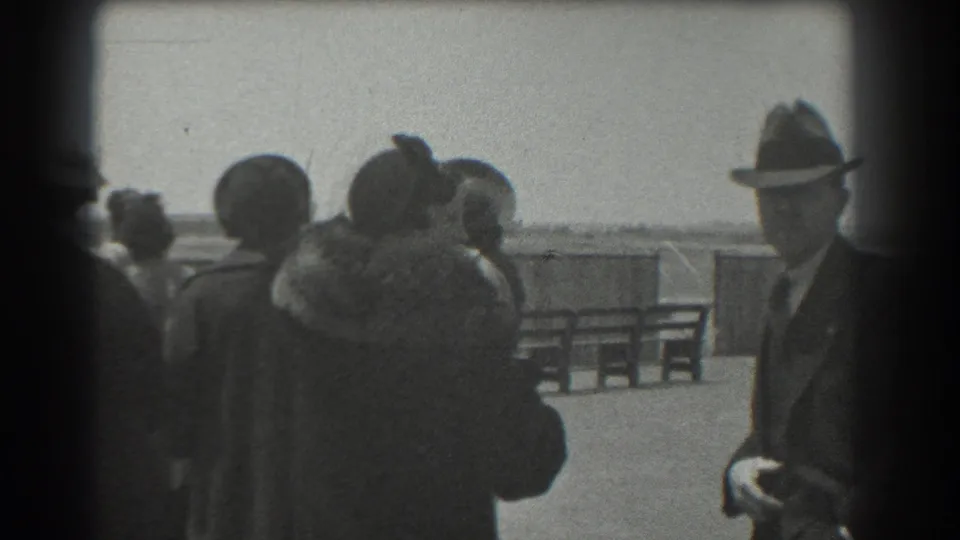 Spectators in coats and hats watch a distant airplane at a San Francisco airfield in 1939 home-movie footage.
