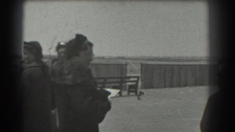 Bundled spectators remain near the airfield railing in grainy 1939 San Francisco black-and-white home-movie footage.