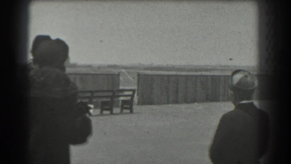 1939 San Francisco home-movie frame showing women in period coats and hats gathered by a railing, looking away from the camera.