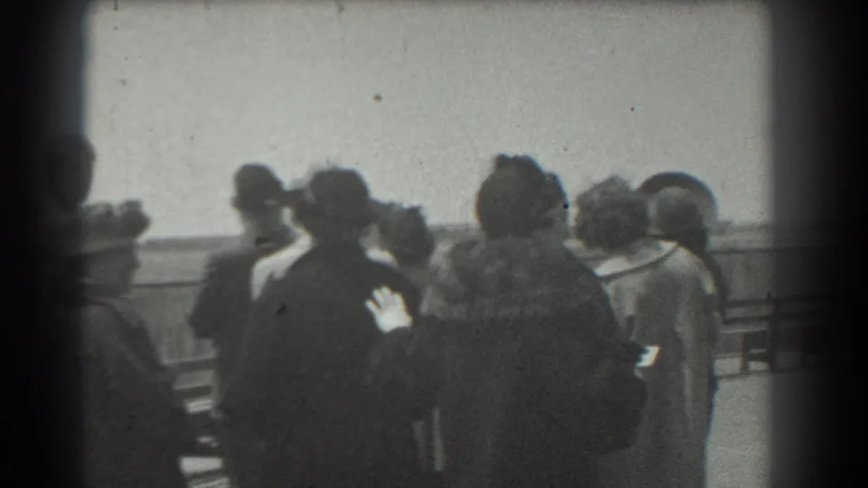 Home-movie frame from 1939 San Francisco showing women in period dress grouped near a railing and looking toward an unseen subject.