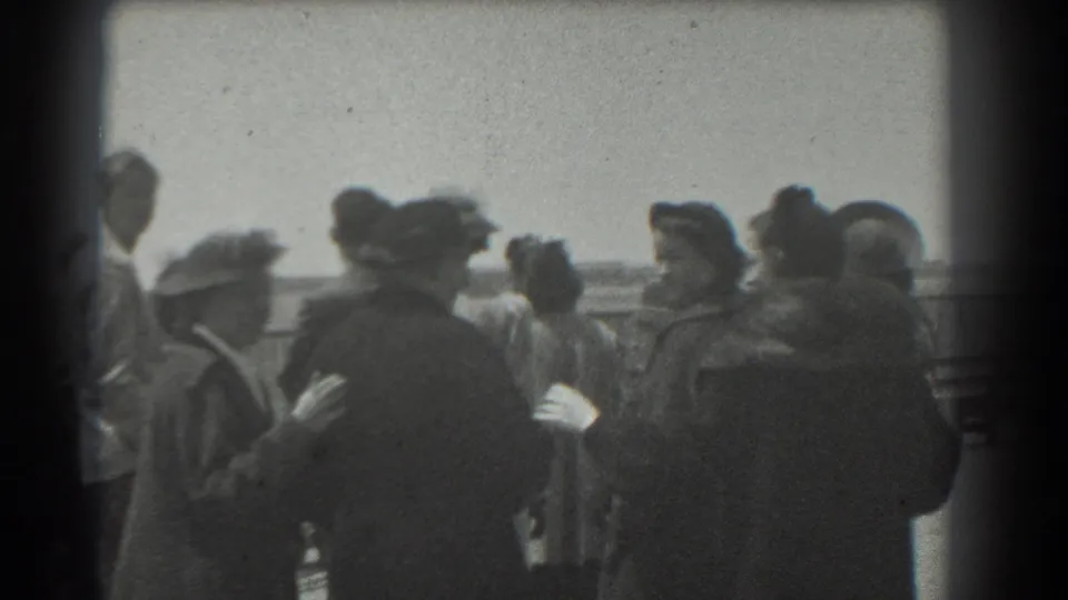 1939 San Francisco waterfront frame with adults in coats and hats standing along a public railing in soft black-and-white 8mm footage.