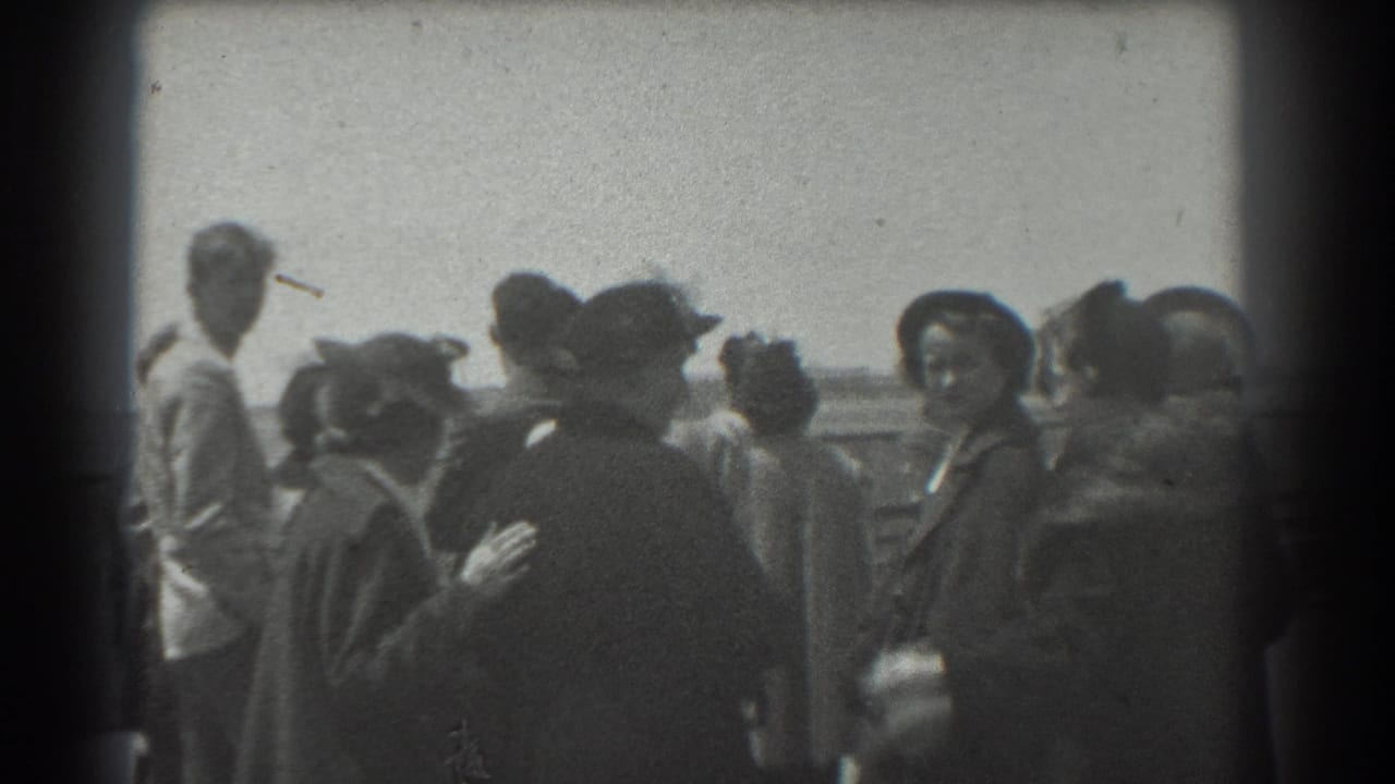 Small outdoor crowd of adults in hats and coats near a railing.