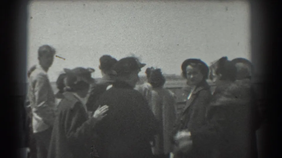 1939 San Francisco home-movie frame showing well-dressed adults in hats and coats gathered outdoors near a railing.