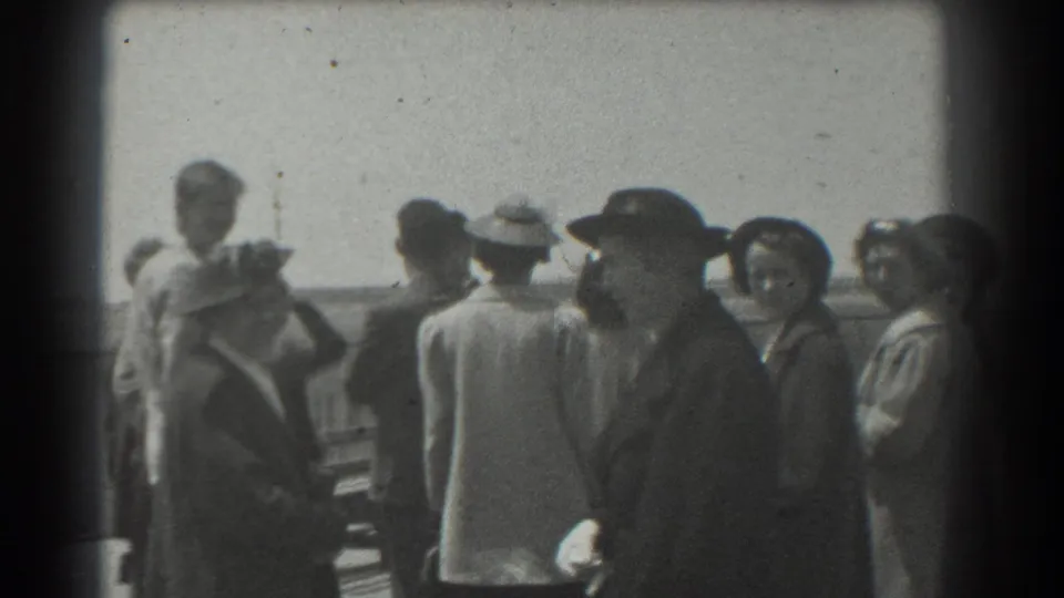 1939 San Francisco home-movie still showing adults in hats and coats clustered near a railing in bright outdoor light.