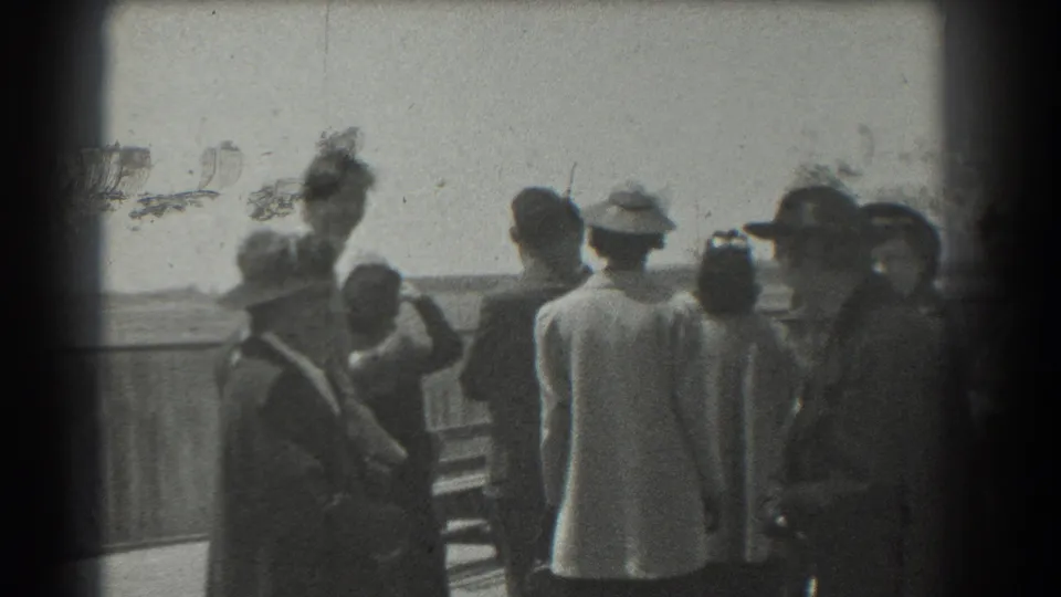 1939 San Francisco frame of adults gathered near a railing, with hats, coats, soft focus, and visible film surface marks.