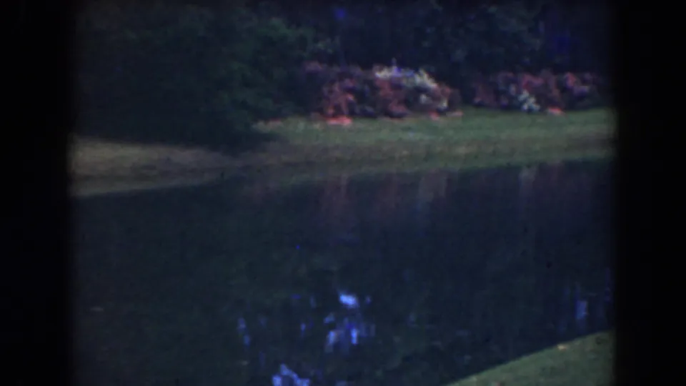 1941 Florida 8mm frame showing a still water channel bordered by grass, shrubs, and dark tree cover.