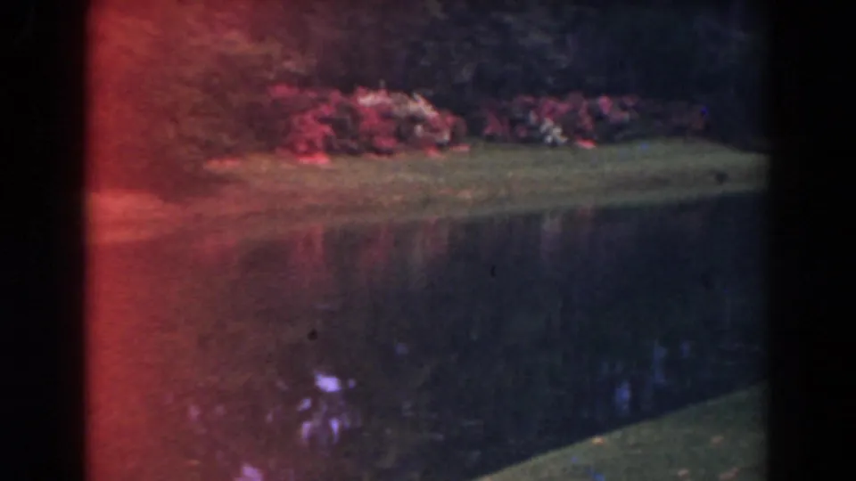 1941 Florida home-movie frame of a landscaped channel, with red color flare and foliage reflected in the water.