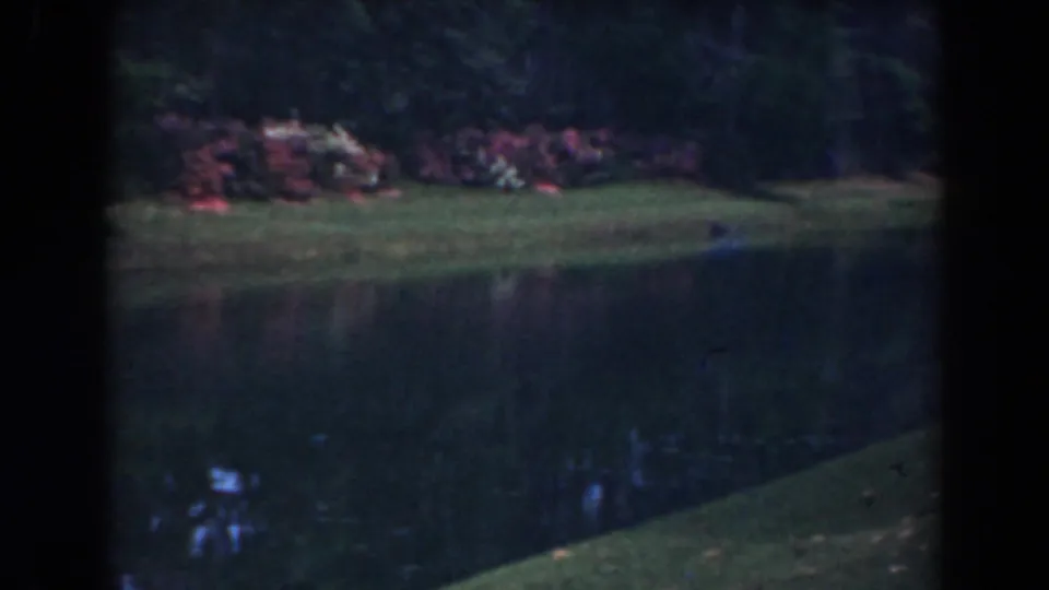 1941 Florida 8mm view of a still channel with grass, low shrubs, tree shadows, and reflective water.