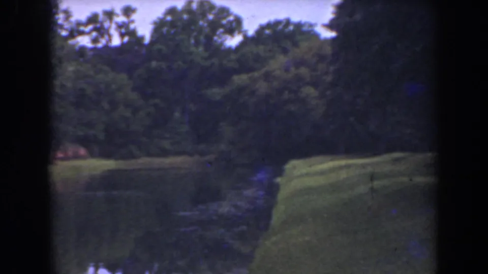 1941 Florida 8mm frame showing calm water, a maintained grassy edge, and a shaded tree line.