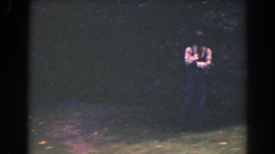 A small figure in a light shirt stands in a dim Florida outdoor scene, framed by heavy grain, dark foliage, and 8mm film borders.