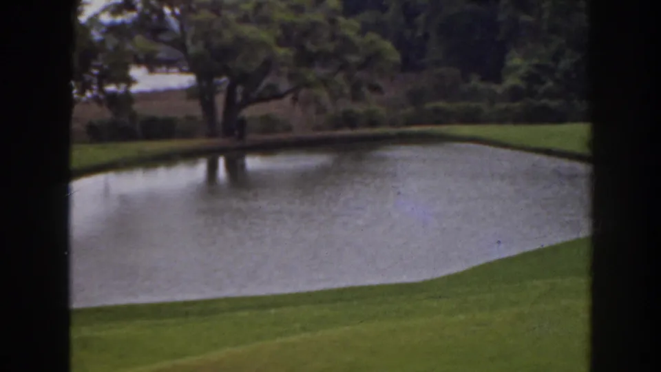 1941 Florida home-movie view of a pond along a manicured golf-course edge, framed by dark vertical bands and trees.