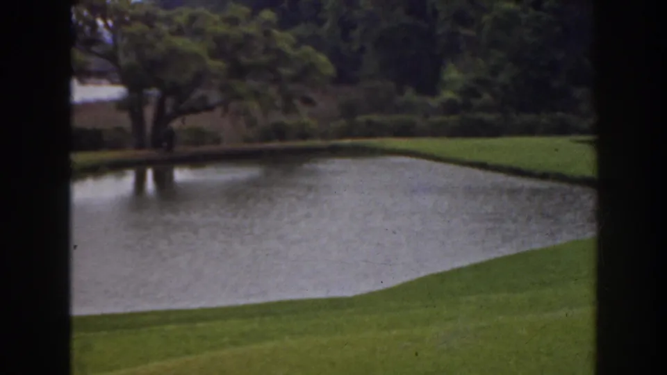 1941 Florida home-movie frame showing a pond, clipped grass, trees, and dark scan edges around the view.