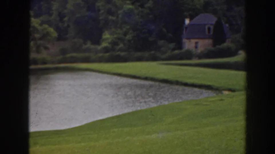 1941 Florida 8mm frame showing a pond foreground and a small dark-roofed stone house set among trees.