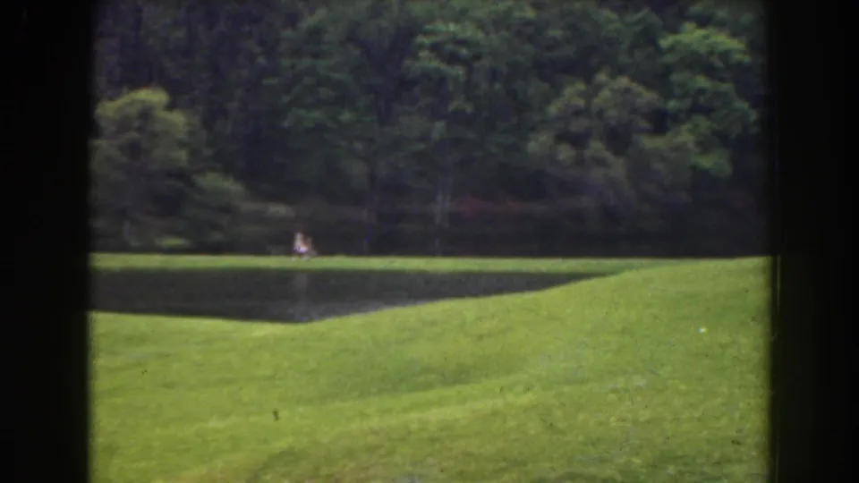 1941 Florida home-movie frame with a small white-clothed figure near the pond, seen across a sloping green field.