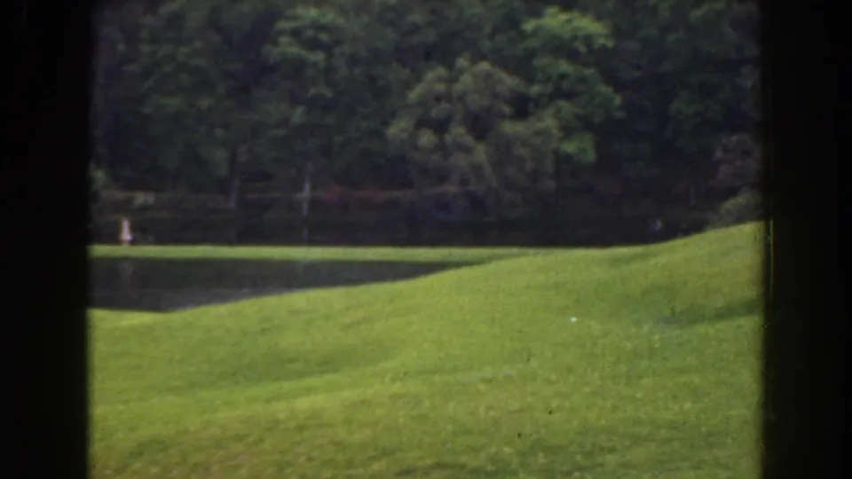 1941 Florida 8mm frame showing a tiny white figure near the left pond edge, with trees and grass filling the view.