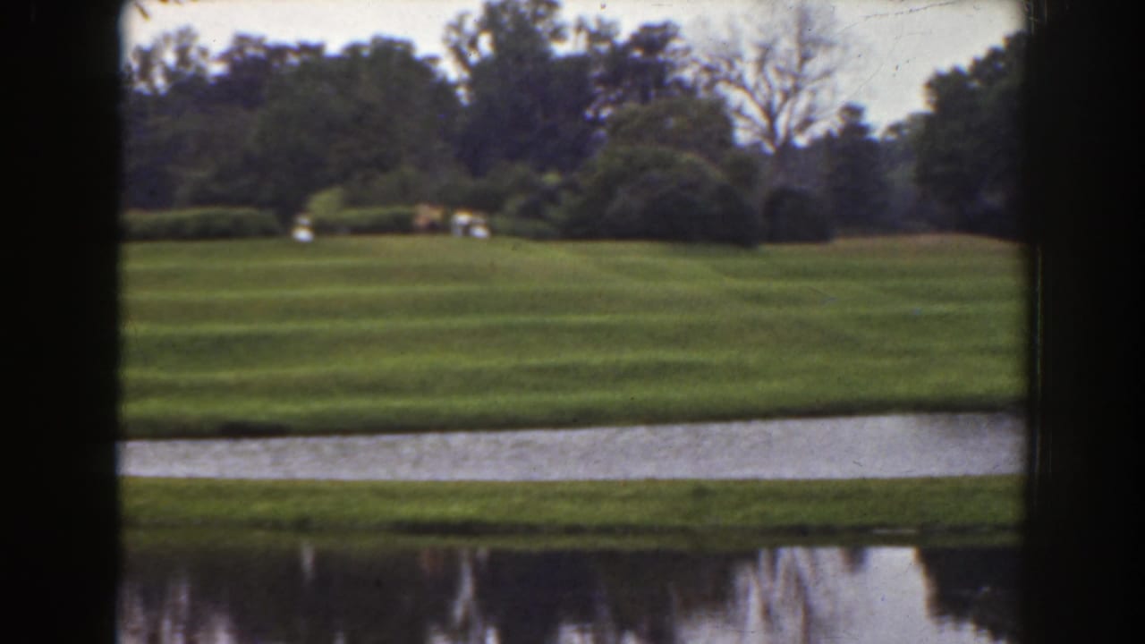 Wide lawn and water with trees, hedges, and distant pale figures.